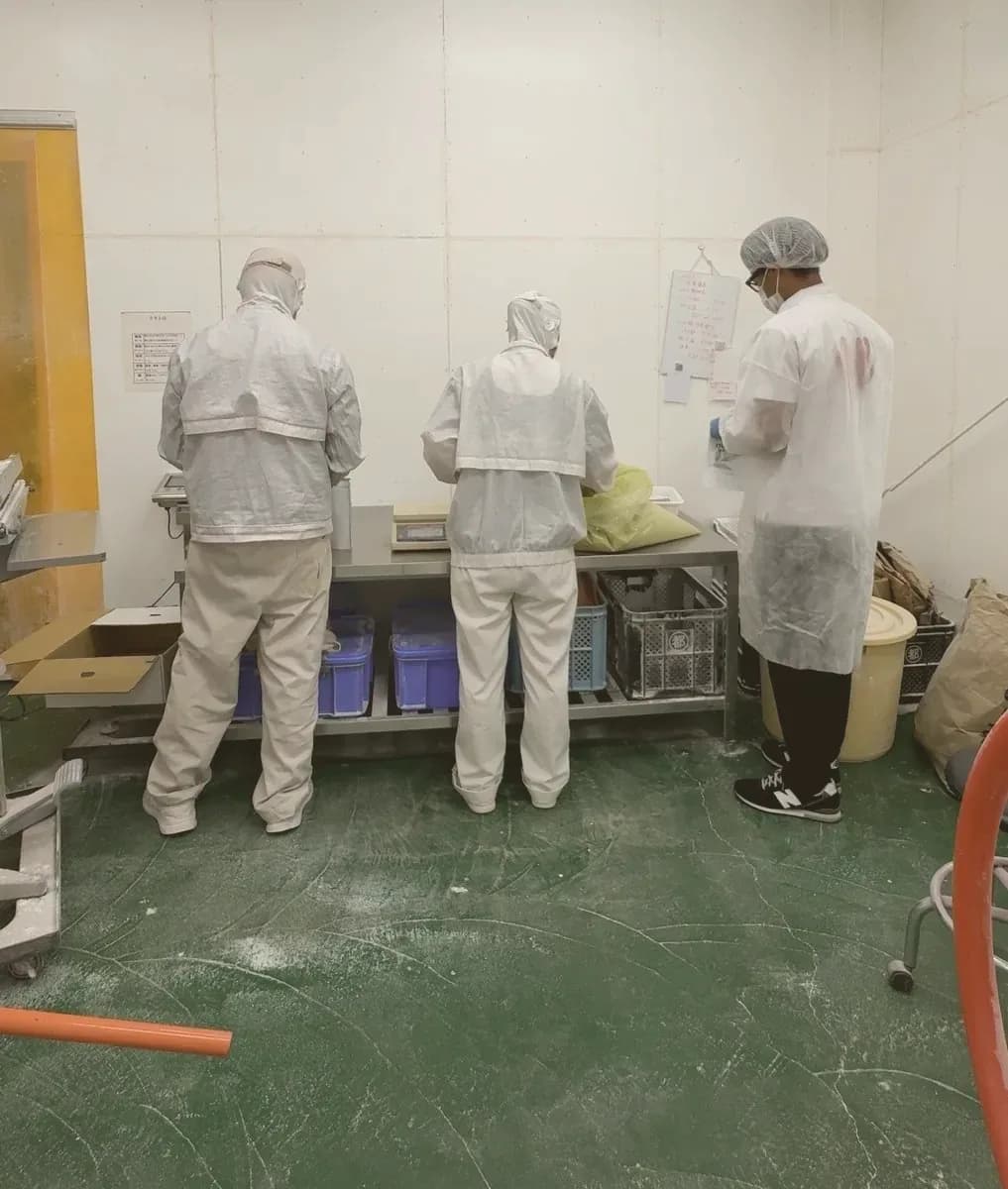 大崎町のさつまいも工場で、白衣姿でパウチを量って封をする南海と2人のスタッフ